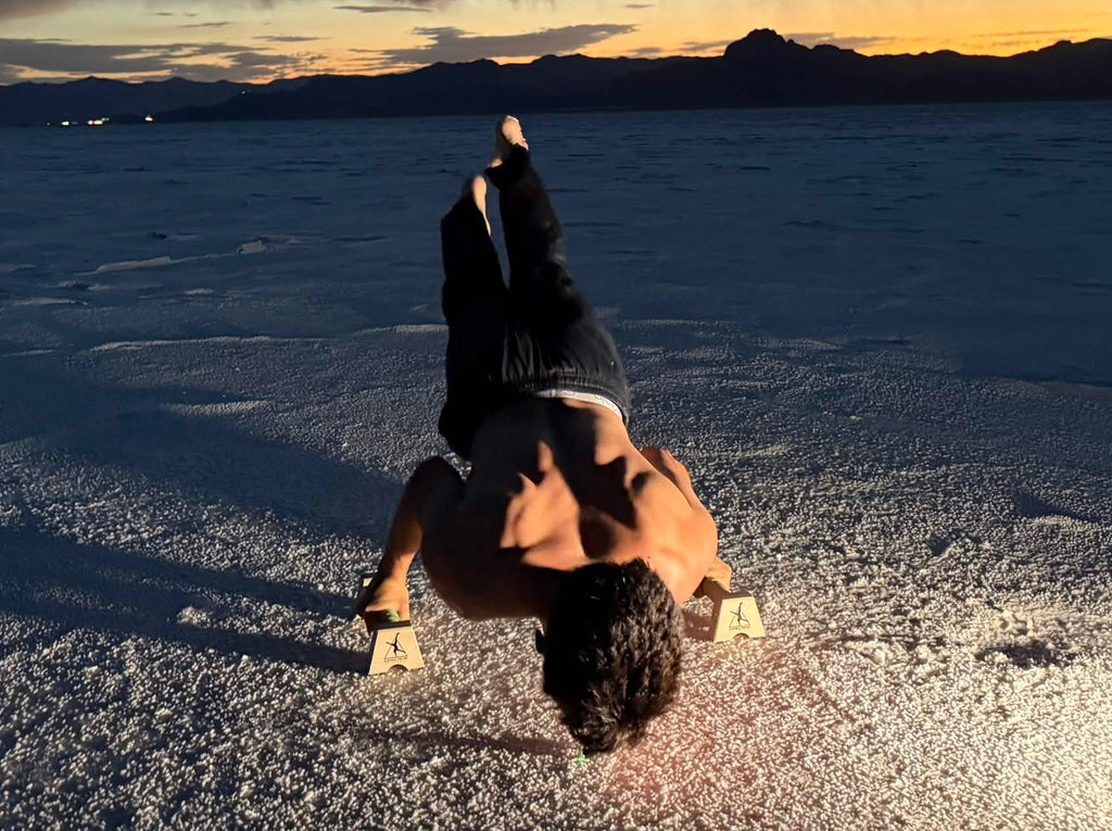 Wide view of an athlete training a planche on Control Theory parallettes on the salt flats at blue hour