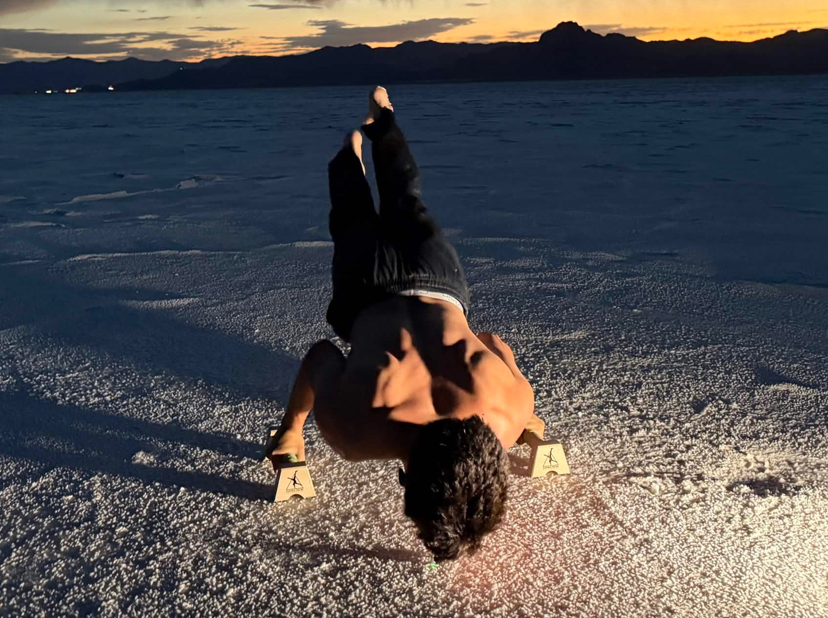 Wide view of an athlete training a planche on Control Theory parallettes on the salt flats at blue hour