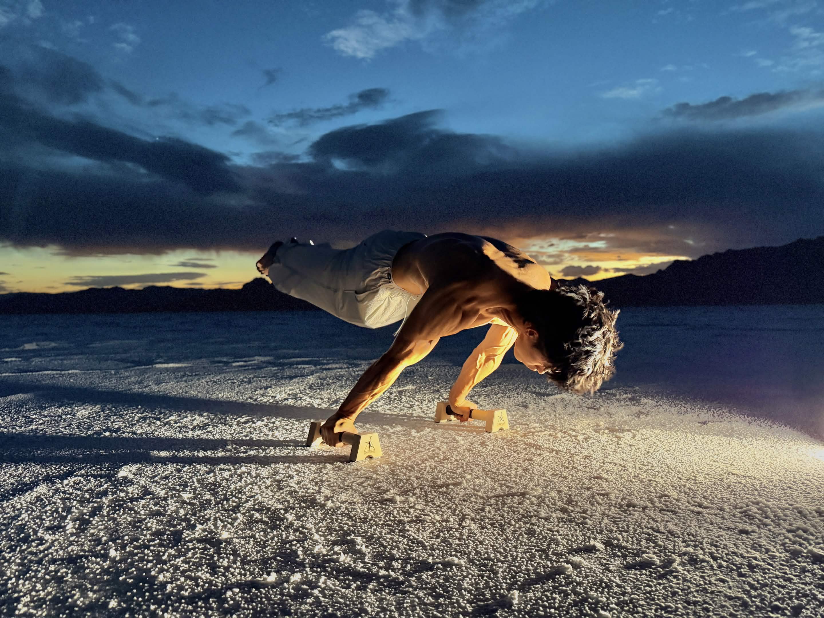 Athlete holding a full planche on Control Theory wooden parallettes on the Bonneville Salt Flats at dusk